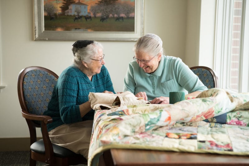 two senior women sewing and laughing together